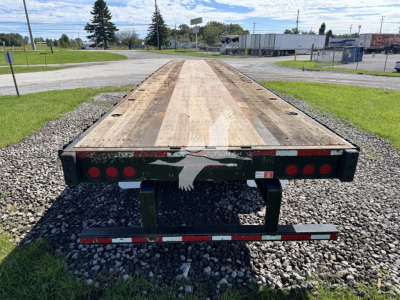 Flatbed trailer rear end showing steel deck and taillights with green undercarriage and reflective bumper.