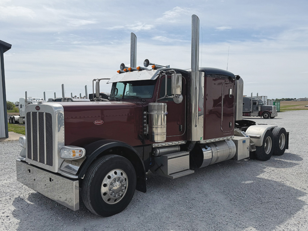 Peterbilt 389 extended hood semi truck with maroon cab, chrome bumper, dual tall exhaust stacks, and front fender details.