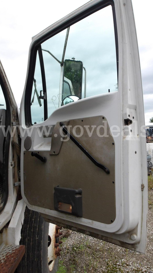 Door interior of a truck cab with beige panel, black window crank, and side mirror reflection visible.