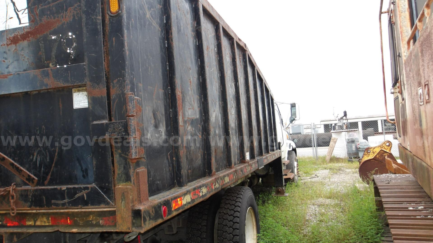 Truck bed side and rear wheel of a used 2006 Sterling Acterra grapple truck in a gravel lot, showing rust around the steel dump bed.
