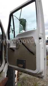 Door interior of a truck cab with beige panel, black window crank, and side mirror reflection visible.