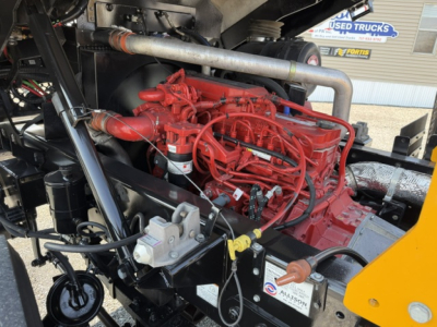 Engine bay view showing a red diesel engine with various hoses and a yellow painted component in a yard truck, with VIN and used tag nearby.