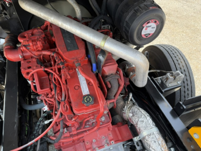 Engine bay of a red Capacity Sabre truck showing diesel engine with intake, hoses, and exhaust, plus a black circular component and metal frame.