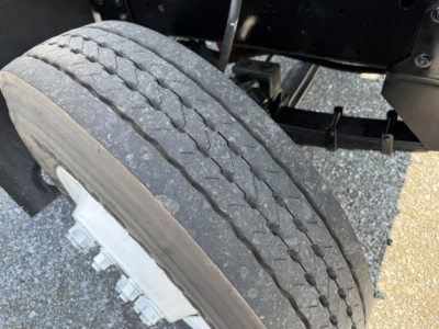 Tire and wheel area of a vehicle chassis showing a single front tire with tread wear and part of the suspension and frame.