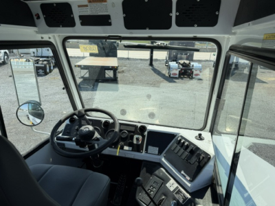 Cab interior of a truck showing steering wheel, dashboard with gauges and switches, large windshield, side windows, and overhead panels.