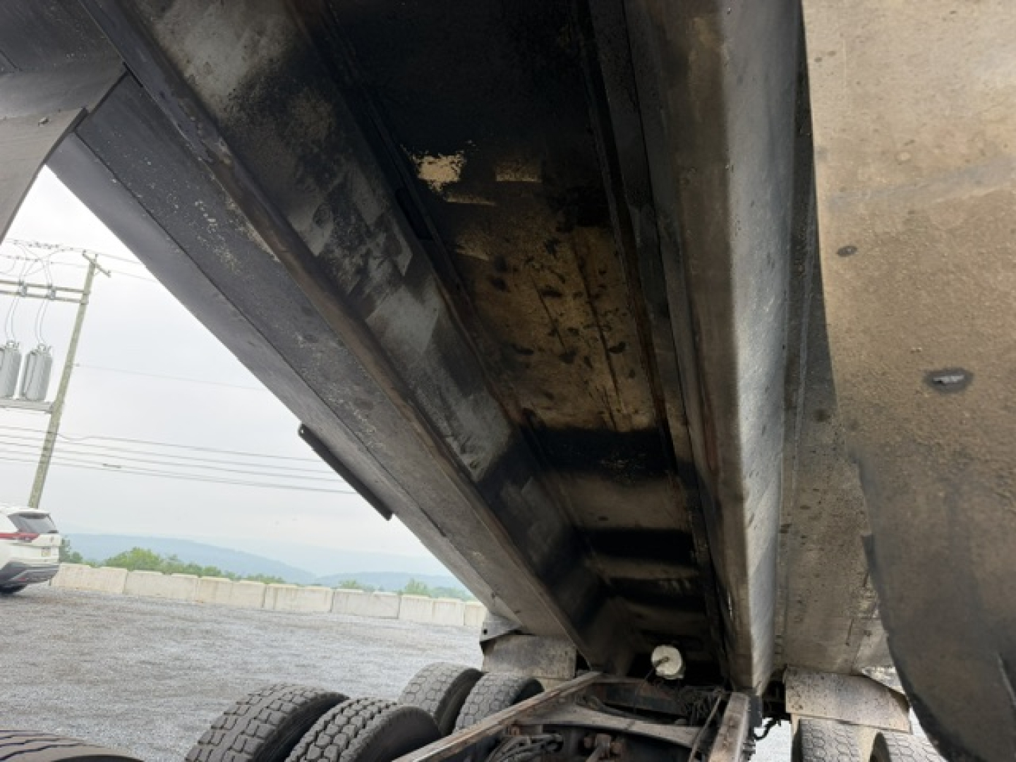 Dump truck underbody showing metal dump bed side and hydraulic mechanism in a raised position.