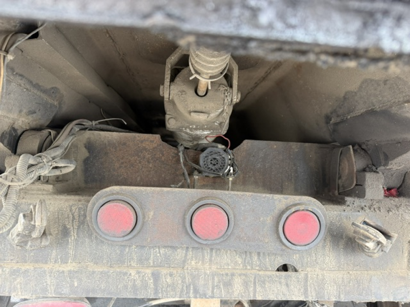 Truck rear view showing three red circular taillights and hitch assembly with frame and wiring under a dirty truck bed.