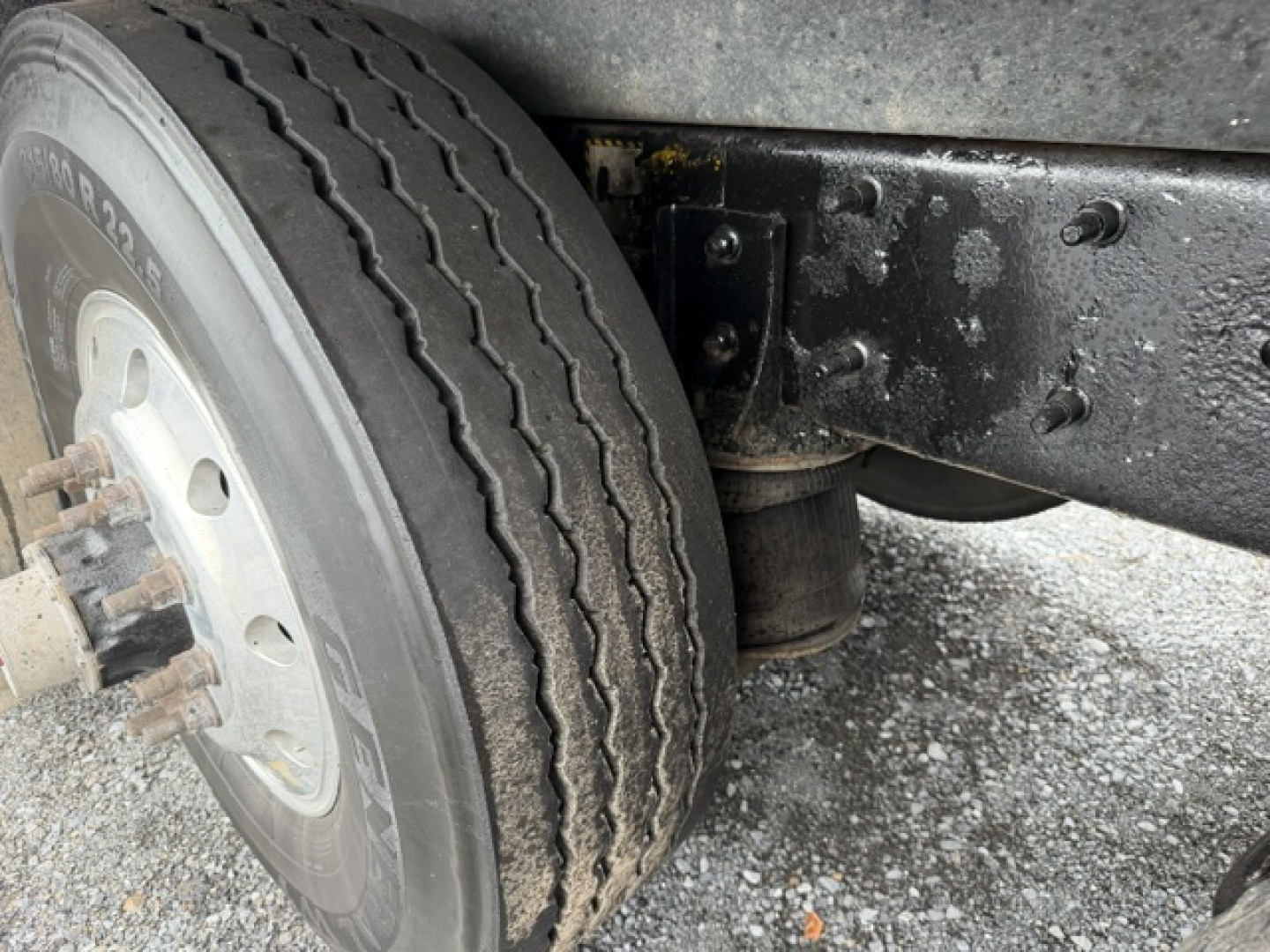 Truck axle close-up showing front dual wheels with tire treads and suspension mounting on a Mack CV713 chassis.