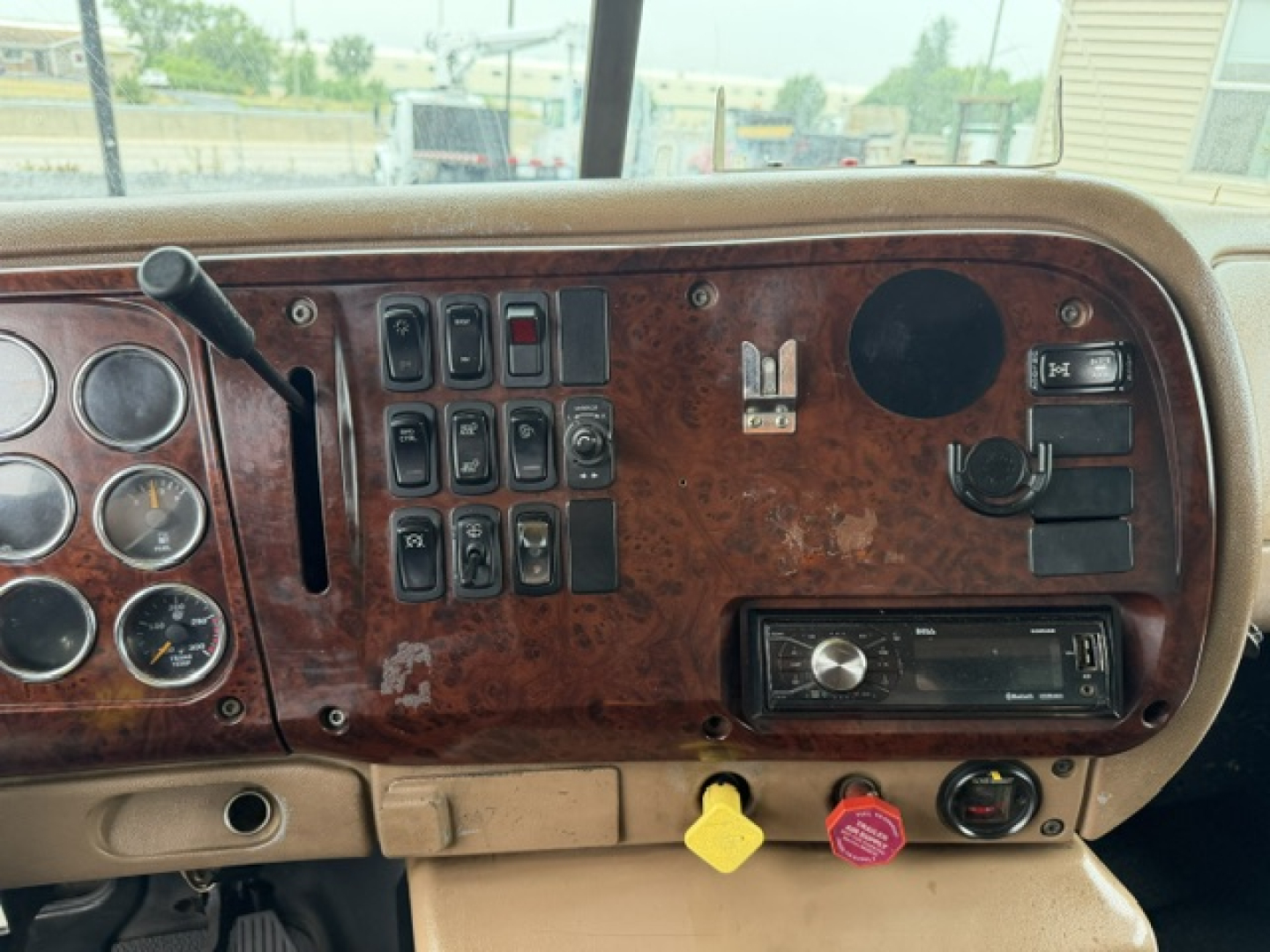 Dashboard interior of a Mack CV713 truck showing switches, gauges, and a radio with wood grain panel.