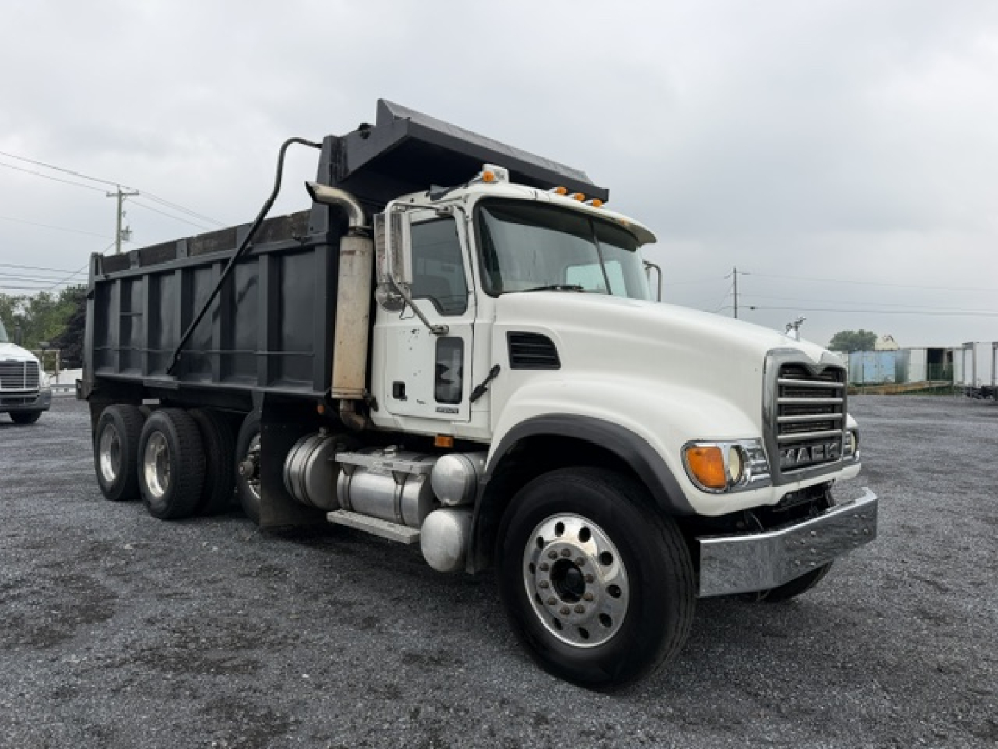 Dump truck with white cab and black dump body, Mack CV713, side view showing front and passenger side, in a gravel lot.