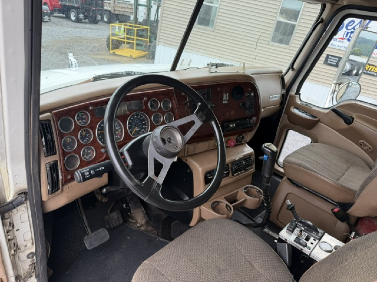 Mack CV713 interior view showing steering wheel and dashboard with numerous gauges and beige seats.