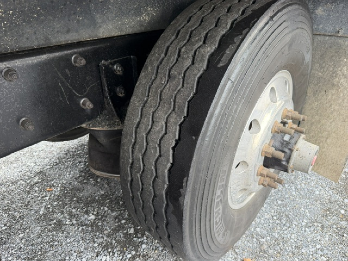 Truck wheel and front suspension of a Mack CV713 dump truck showing a dual rear? Actually front axle with single tire, wheel hub with lug studs and brake drum. No legible labels.