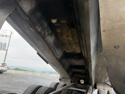 Dump truck underbody showing metal dump bed side and hydraulic mechanism in a raised position.