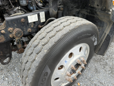 Truck front wheel and engine bay of a 2007 Mack CV713 dump truck showing tire, hub, and wheel assembly.