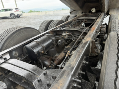 Chassis center view showing truck frame and driveline components under a Mack CV713 dump truck, including leaf springs, drive shaft, suspension, and rear wheels.