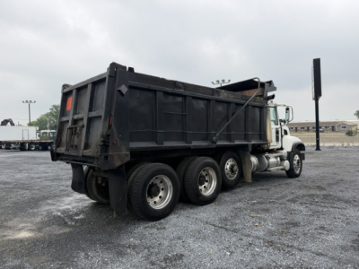 Dump truck rear three-quarter view showing cargo bed and dual rear axles on a white cab chassis.