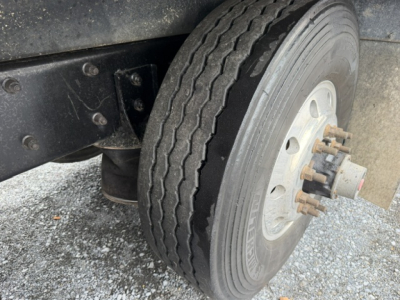Truck wheel and front suspension of a Mack CV713 dump truck showing a dual rear? Actually front axle with single tire, wheel hub with lug studs and brake drum. No legible labels.