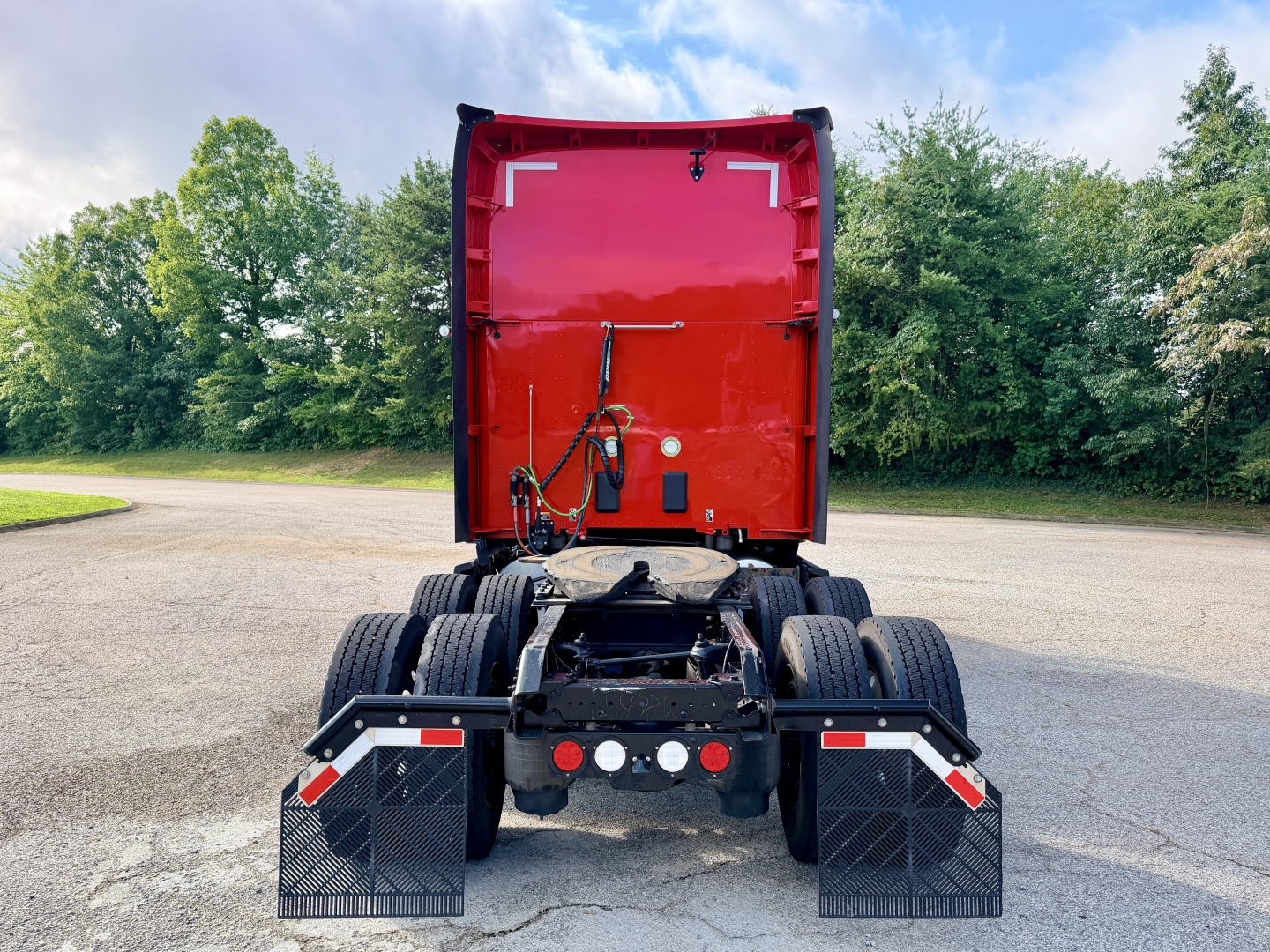Kenworth T680 truck rear view showing fifth wheel and dual rear axles, black mud flaps, red sleeper cab back, and wiring harnesses.