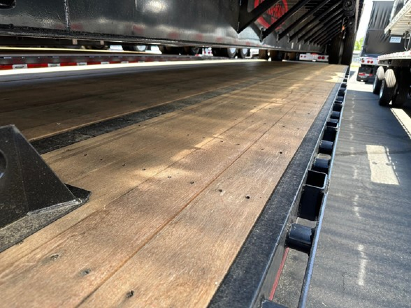 Drop deck trailer bed with wooden planks and steel edge rails, view from side showing platform texture and trailer components.