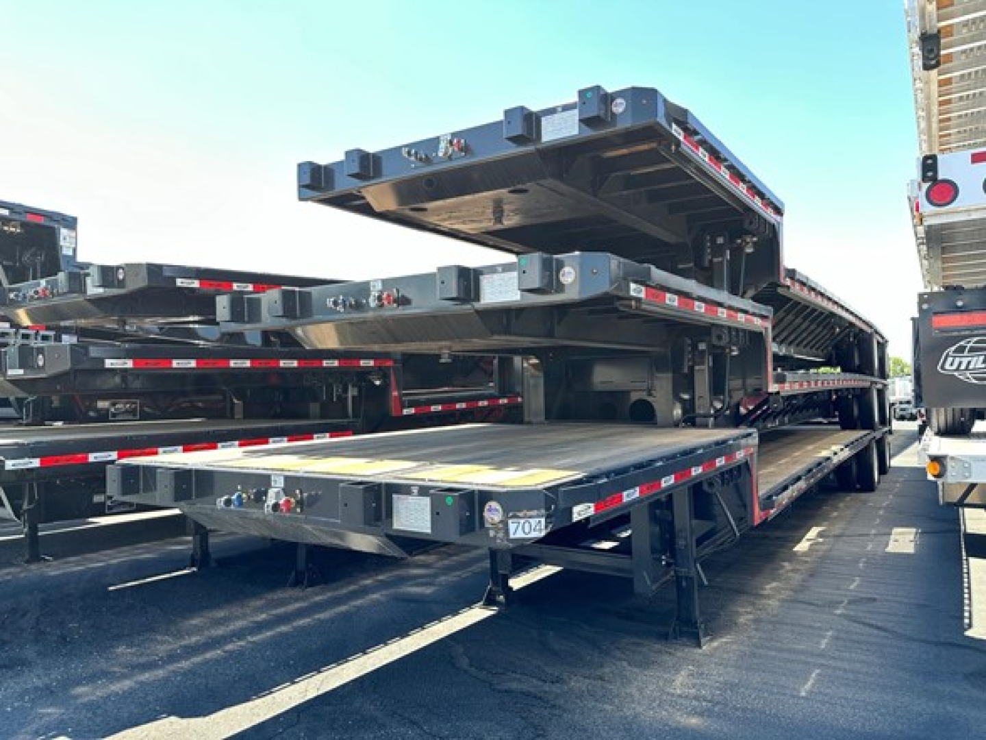 Trailer deck stack showing multiple flatbed sections in a hauler yard with a bright sky