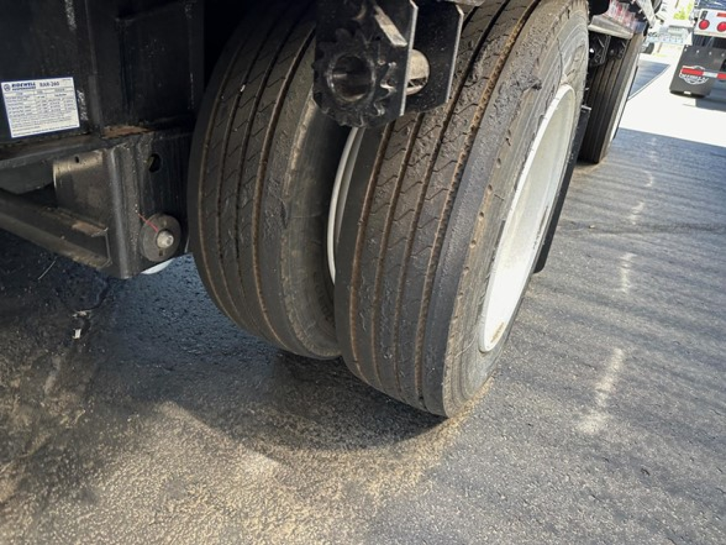 Trailer wheel close-up showing dual tires and white wheel rims on a drop deck trailer.