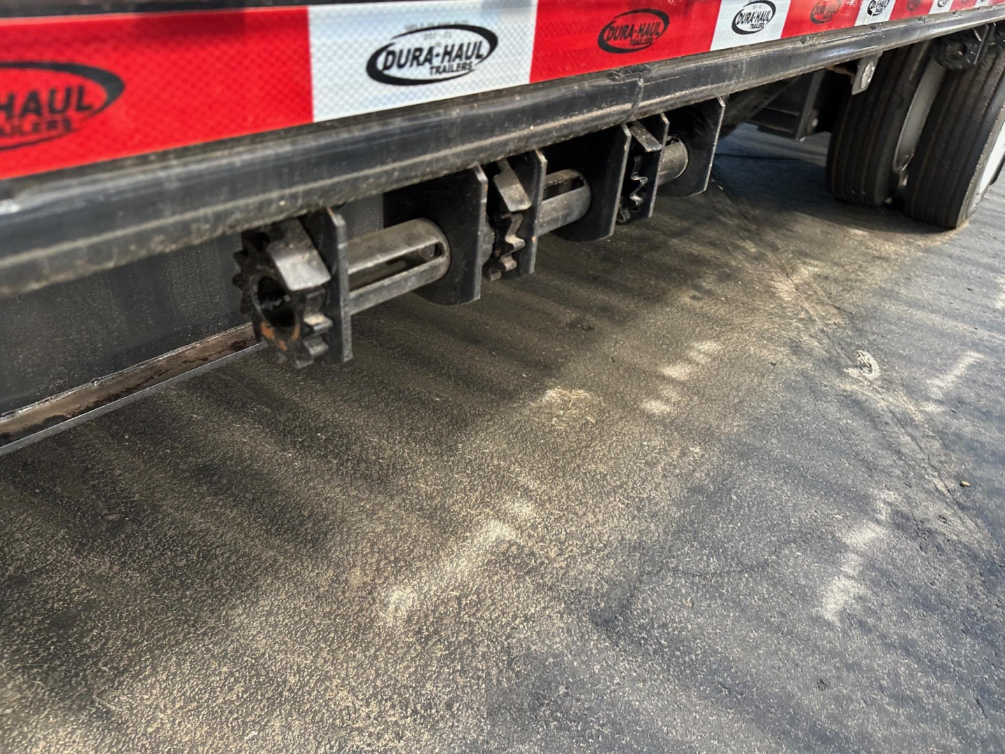 Drop deck trailer underside showing three vertical latching hardware and black frame with red reflective tape along side