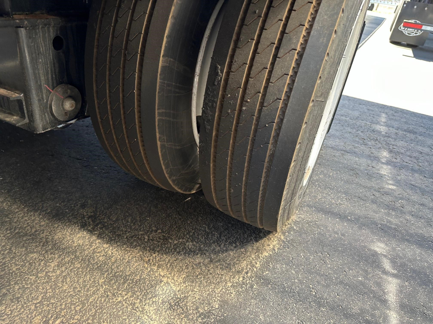 Trailer wheel end showing multiple layered tires and frame components of a drop deck trailer.
