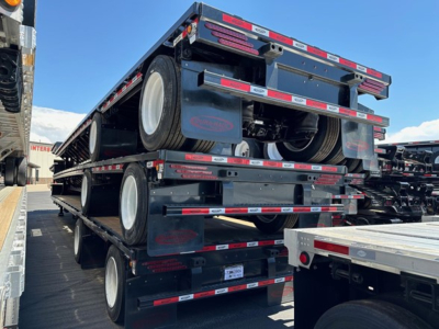Trailer showing multiple stacked drop deck trailers with black paint and red/white reflective tape.