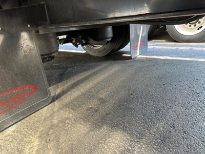 Drop deck trailer underside view with mud flaps and tires visible, showing wheel and suspension area.