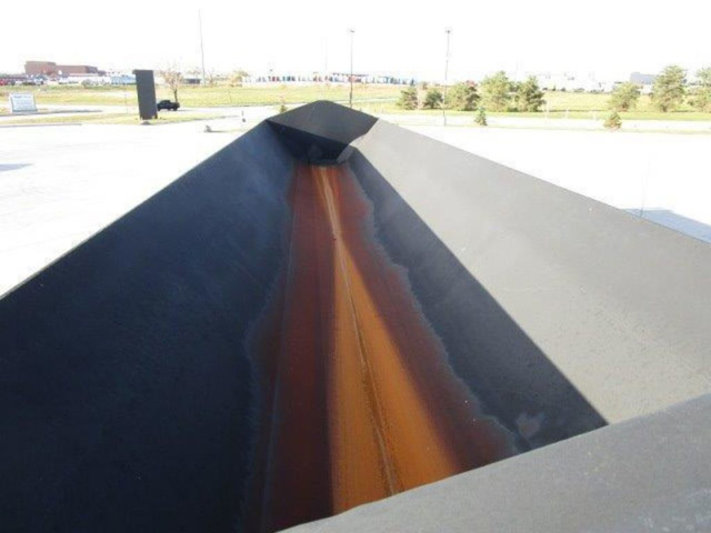 Dump trailer bed interior showing a central rust-colored seam along the raised and angled bed panels.