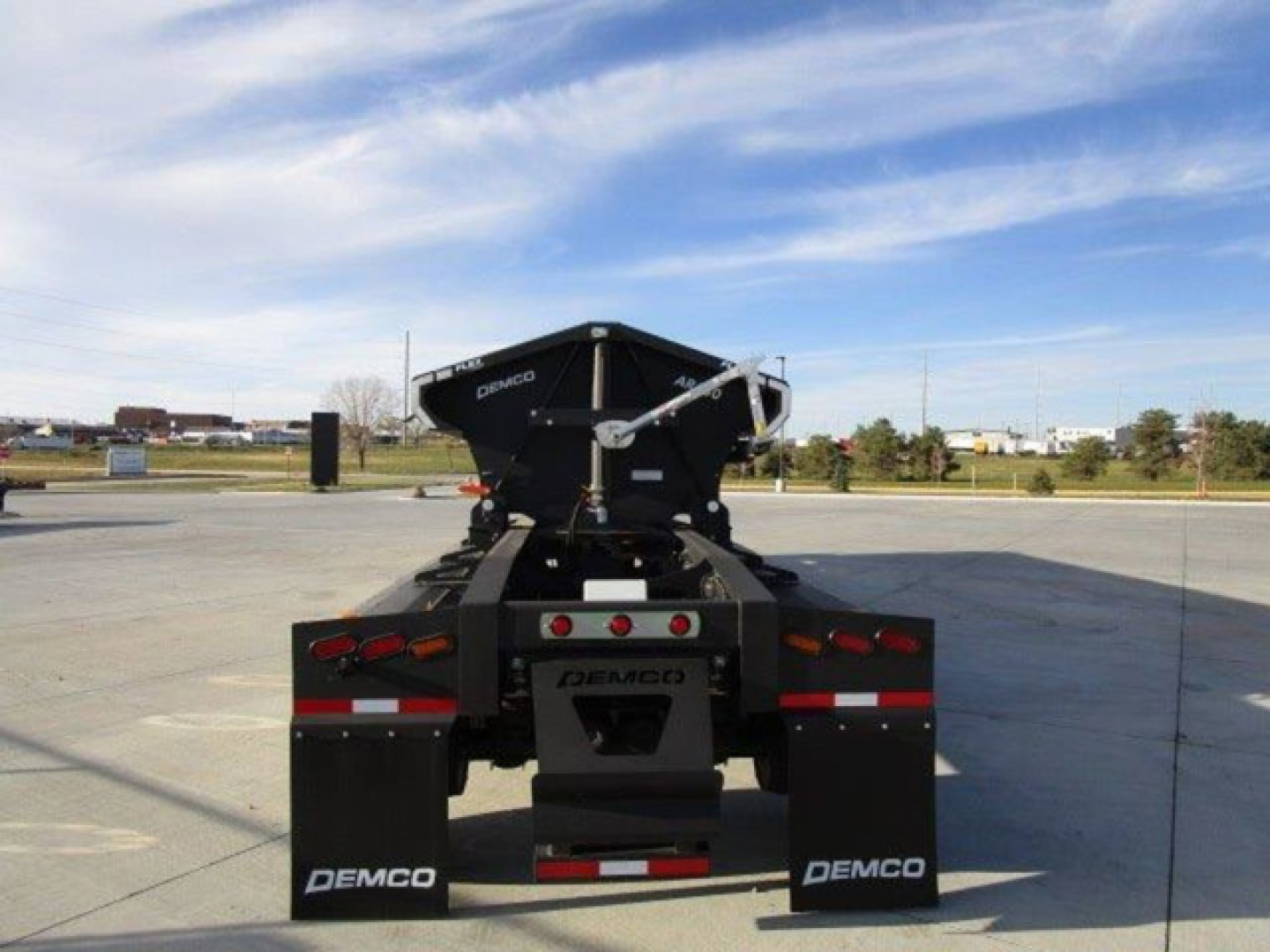 Demco dump trailer viewed from rear showing black hopper and rear steel frame with 'DEMCO' branding and taillights.