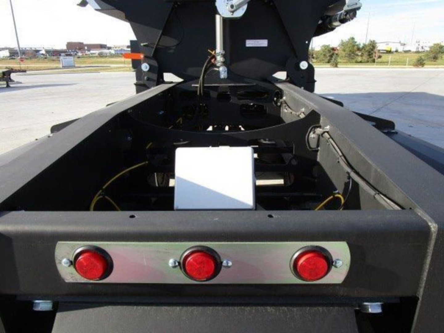 Dump trailer chassis rear view showing three red taillights on a metal plate and the hitch area