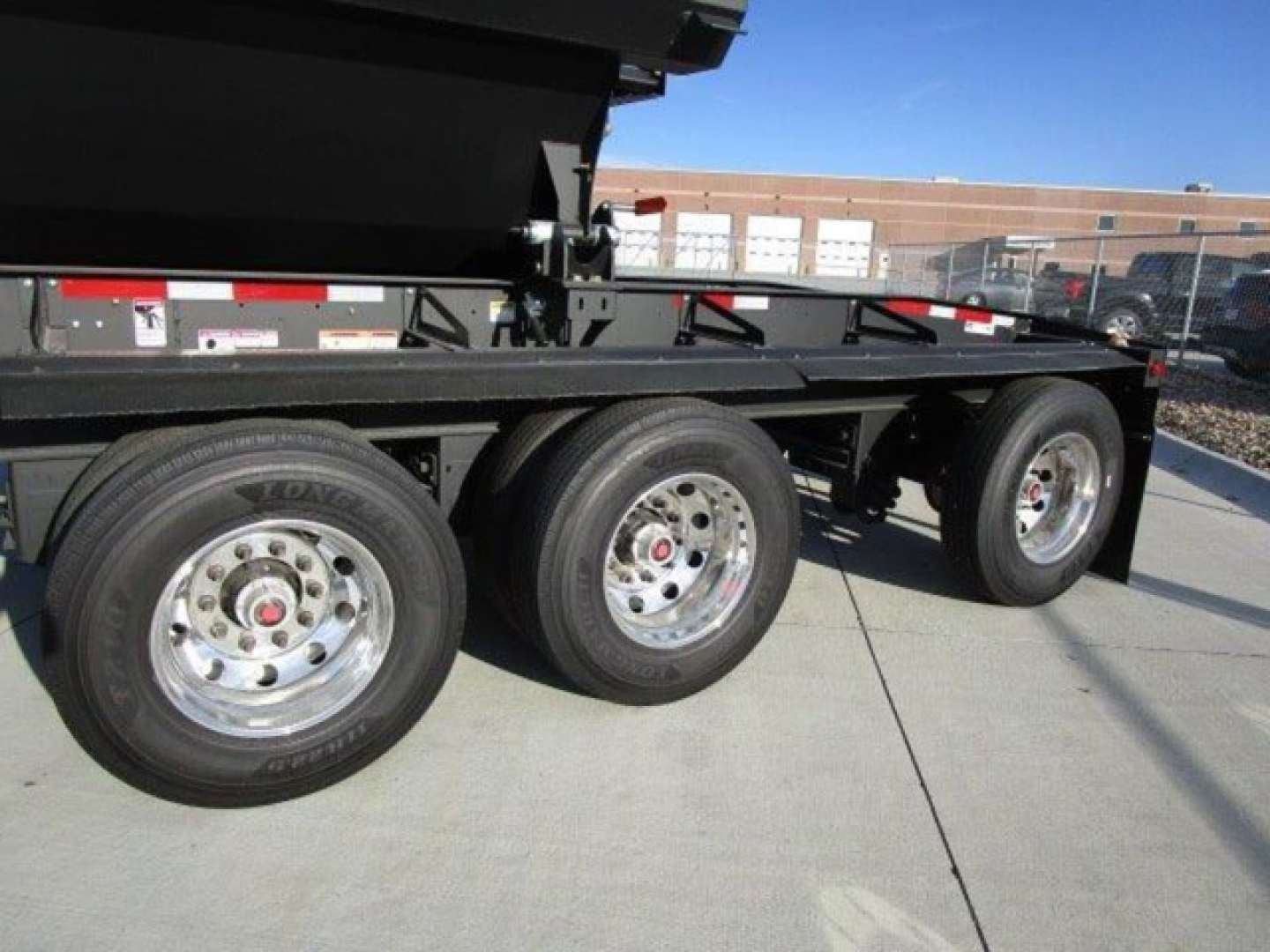 Demco dump trailer showing triple-axle configuration with polished chrome wheels and black dump bed side view.