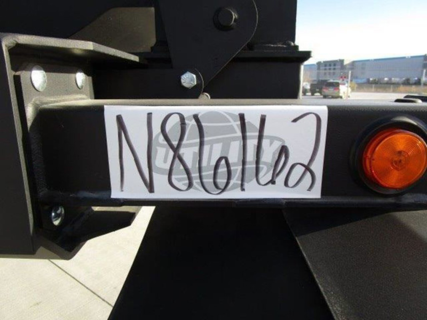 Trailer hitch area of a 2026 Demco dump trailer showing a plate with handwritten VIN tag and a circular orange taillight.