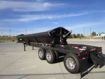 Demco dump trailer with powder-coated frame and dual-axle configuration, side rails, and rear drop-down tailgate. Brand name Demco visible on components; blue sky and dealership lot in background.