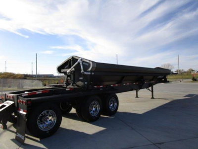 Demco dump trailer in view showing triple-axle configuration with a folded hydraulic hoist and dump bed, black with silver components.