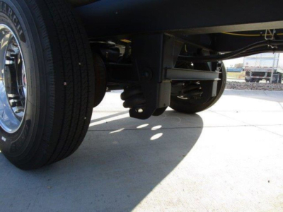 Dump trailer undercarriage showing suspension and dual rear wheels with leaf springs and hydraulic components visible.