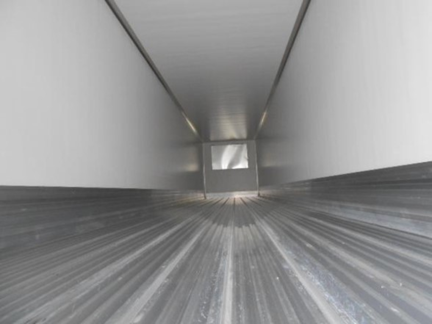Trailer interior showing long refrigerated cargo area with ribbed metal floor and side walls, view toward rear door opening