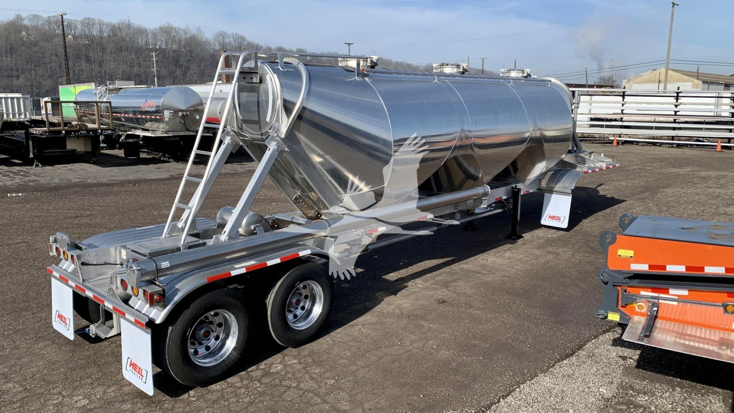 Trailer tanker: new Heil cementer pneumatic dry bulk trailer with polished stainless steel tank on tri-axle tandem, rear ladders and safety rails, parked in yard.