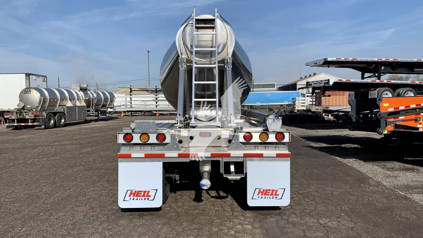 Rear view of a new Heil cementer pneumatic dry bulk trailer showing rear bumper, lights, and dual HEIL sponsor mud flaps. Visible text includes VIN and stock details though not on the trailer itself.