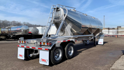 Heil Cementer pneumatic dry bulk trailer in chrome finish with dual rear axles and rear spreaders, tanks and ladder visible.