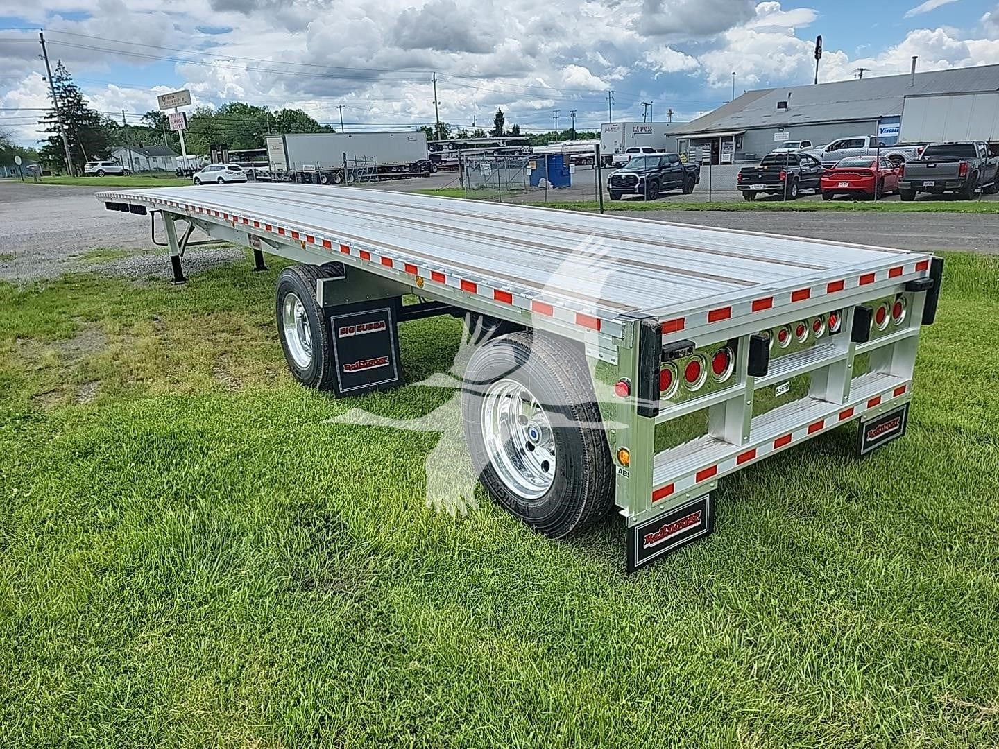Flatbed trailer by Reitnouer with aluminum deck, dual rear axles, and trailing edge wall; reflective tape along sides; stock number VR080772.