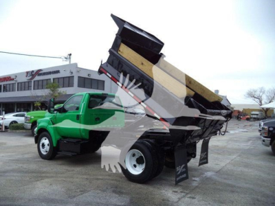 Dump truck bed raised on a green Ford F-650 SD in a dealership lot with a lifted dump box and white wheels.