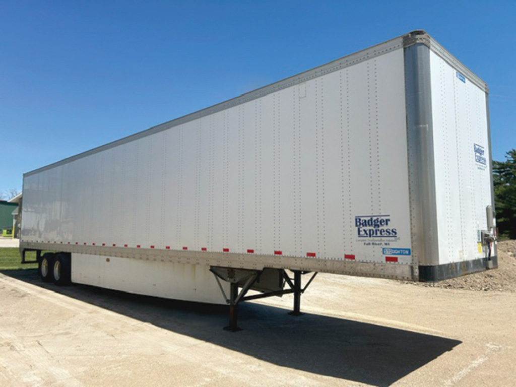 Trailer undercarriage and side view showing 2018 Stoughton van trailer with Badger Express sticker and label, elevated landing gear, white exterior.