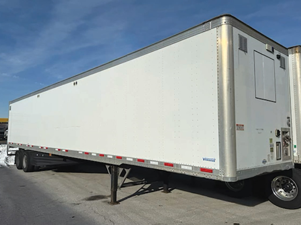Vanguard aluminum box trailer side view with landing gear extended and rear access door visible, white exterior and logo near back corner.