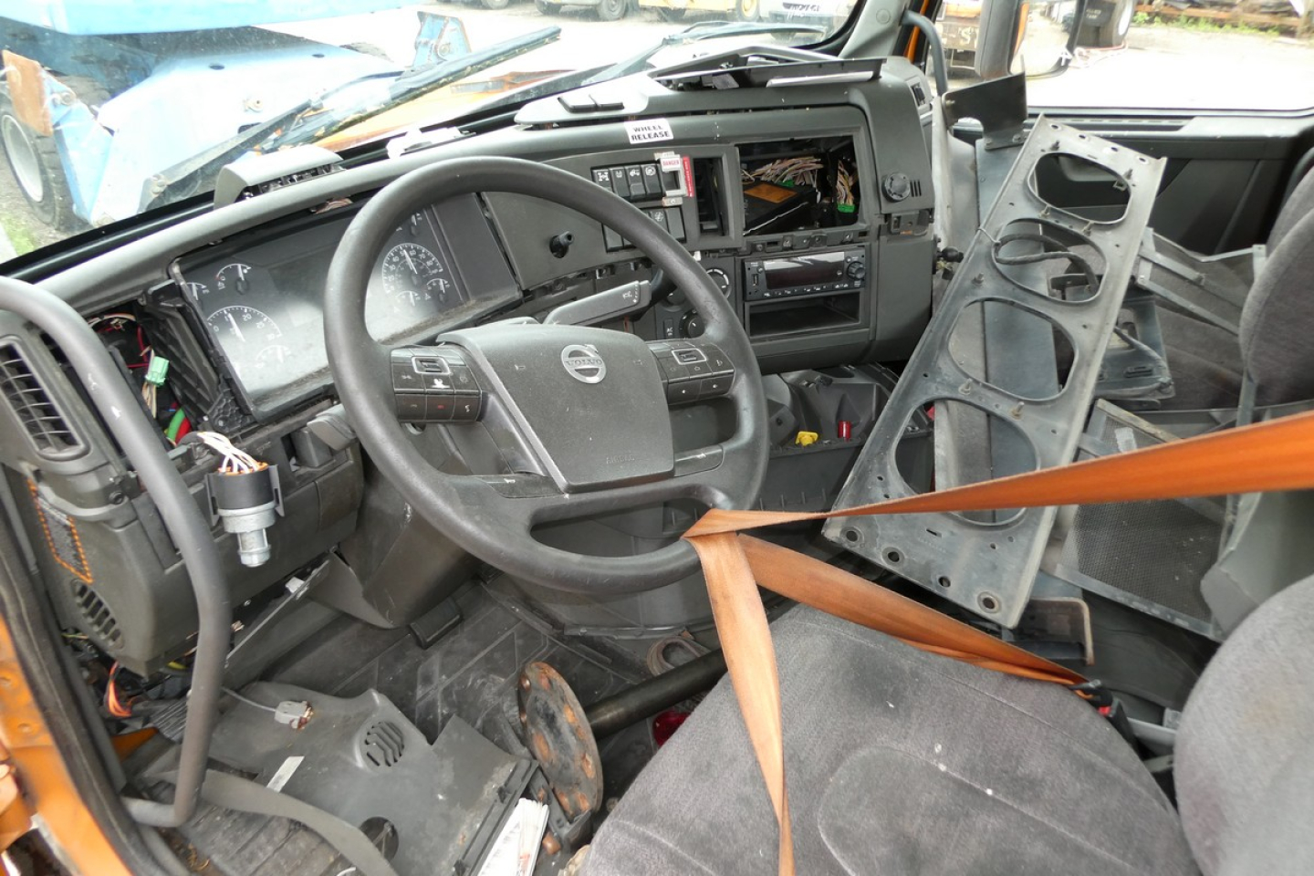 Interior of a Volvo VNR truck cabin showing steering wheel, dashboard, exposed wiring, and loose components with a seat belt hanging across.