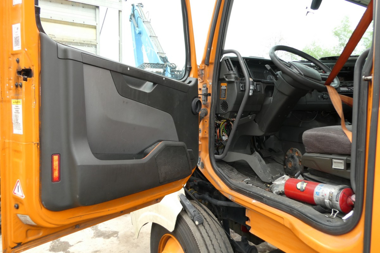 Volvo VNR truck cab interior and open door showing steering wheel and driver's seat with orange exterior.