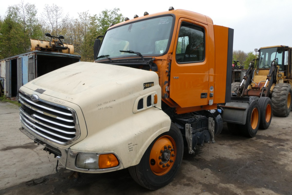Truck cab and chassis of a 2019 Volvo VNR64T300 dual-tone color with cream front and orange sleeper, side view showing front grille and wheel; VIN visible on listing.