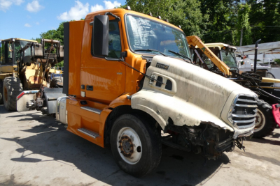 Volvo VNR64T300 cab and front chassis showing damaged right front fender and hood with visible windshield and side mirror, orange cab, junkyard background