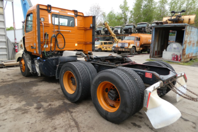 Volvo VNR64T300 tractor show chassis and orange cab with dual rear axles and spare wheel, visible in a yard with other trucks.